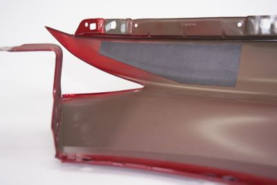 Close up of pre-formed structural patch installed on a red painted car body used to fill open areas and seal open gaps, on a white background