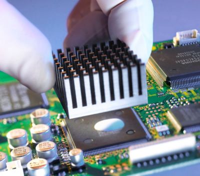 Photo of white gloved technician attaching heatsink to top integrated circuit with thermally conductive adhesive