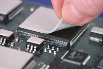 Photo of light grey  thermal gap pad being placed on top of an electronic component on a pcb with other light grey thermal gap pads on other components elsewhere on the pcb assembly