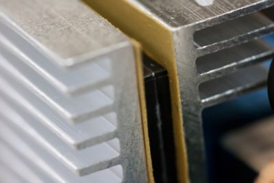 Close up photo of electronic component sandwiched between two metal heat dissipation fins and bonded to the metal fins with a thermal interface material