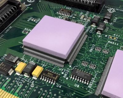Photo of light purple thermal interface material on top of electronic components on a green pcb