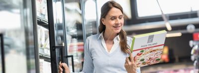 Woman reading the contents of a pizza box in the freezer section of the grocery store