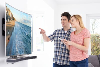Photo of young couple standing next to a wall mounted curved television screen shutterstock ID 424840117